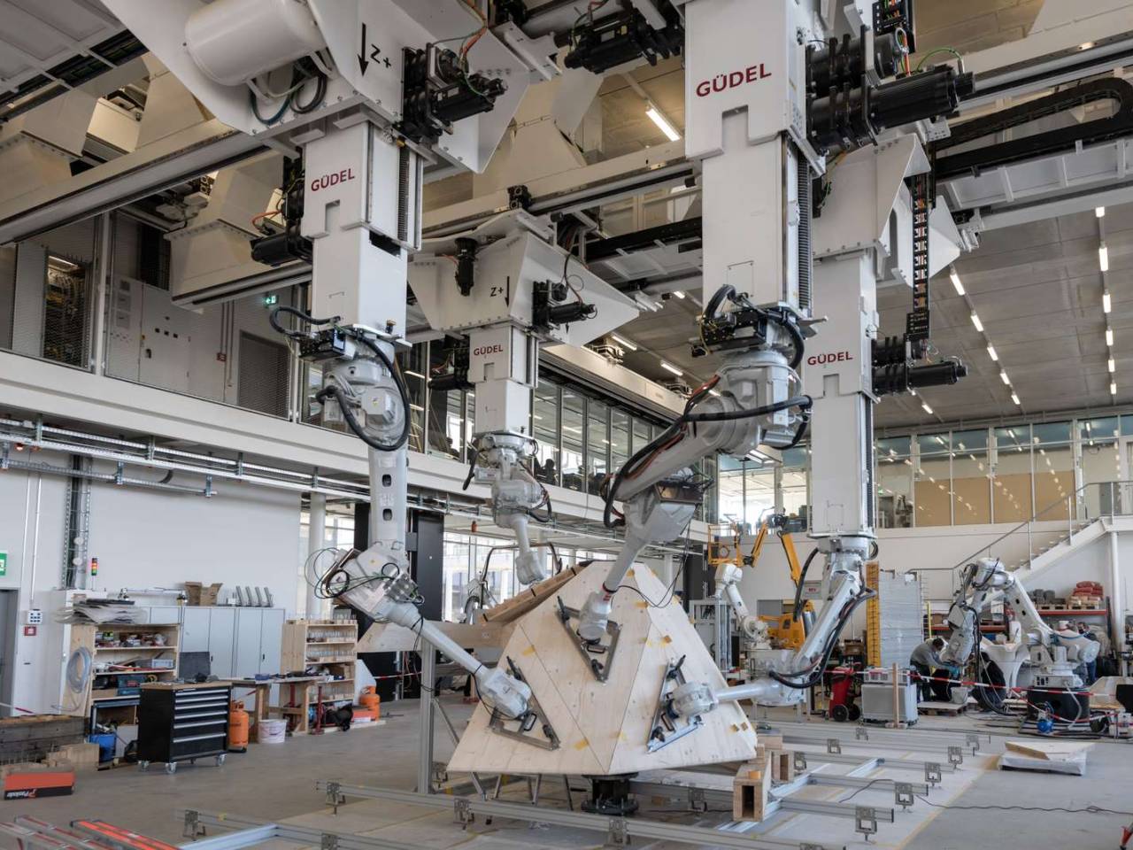 Im Gleichtakt nehmen vier hängende Roboterarme die ihnen zugewiesene Holzplatte auf